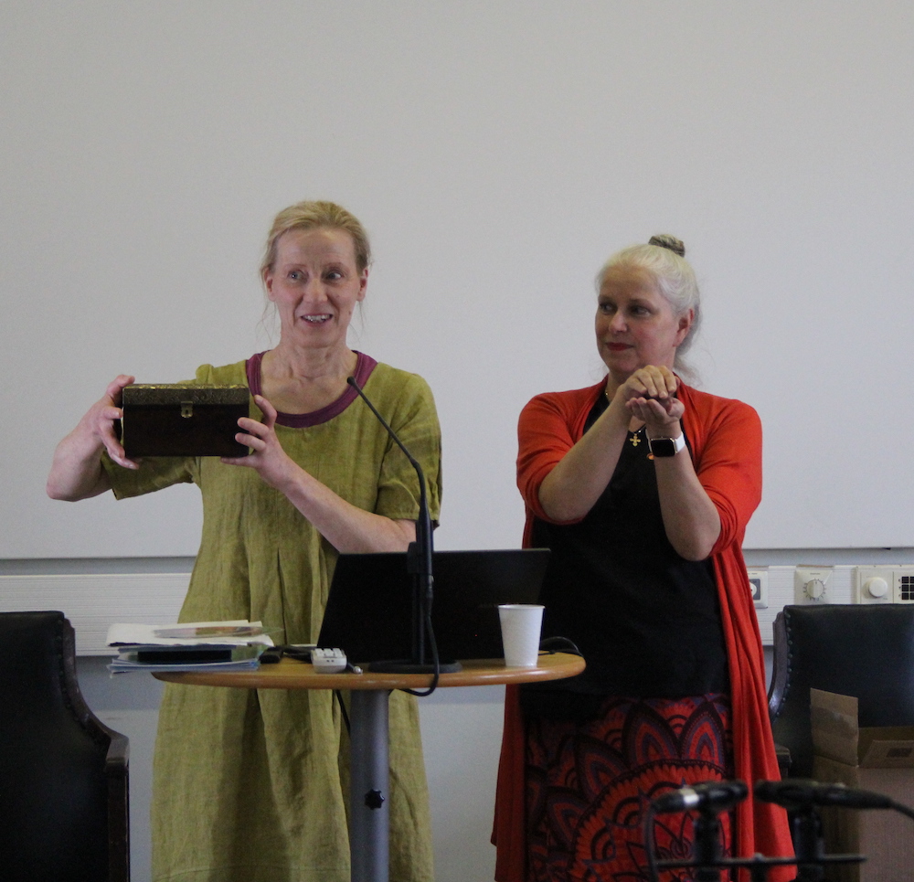 Kuvassa seisovat vierekkäin Mikaela Molander ja Ulla Sergejeff. Ullalla on päällään punainen paita ja kädet tuotu eteen supuksi kuvastamaan arkkua. Mikaelalla on päällään vihreä mekko ja kädessään hän pitelee pientä arkkua.