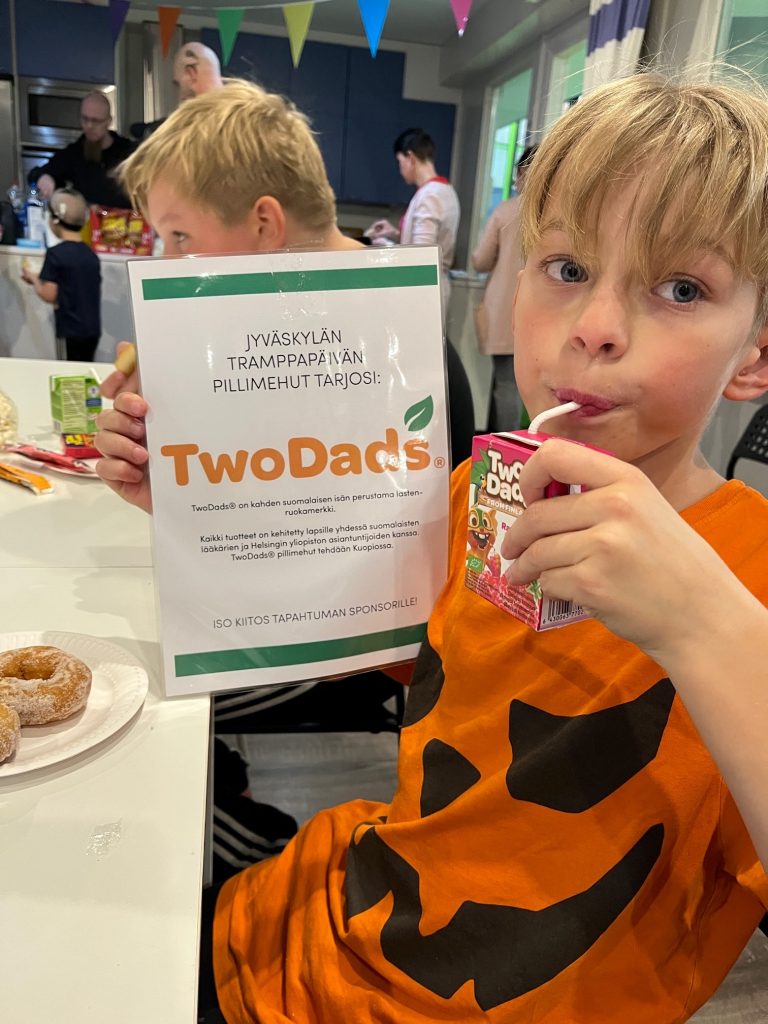 Kuvassa poika juo TwoDads-pillimehua ja pitää kädessään plakaattia, jossa on tietoa TwoDads-pillimehuista