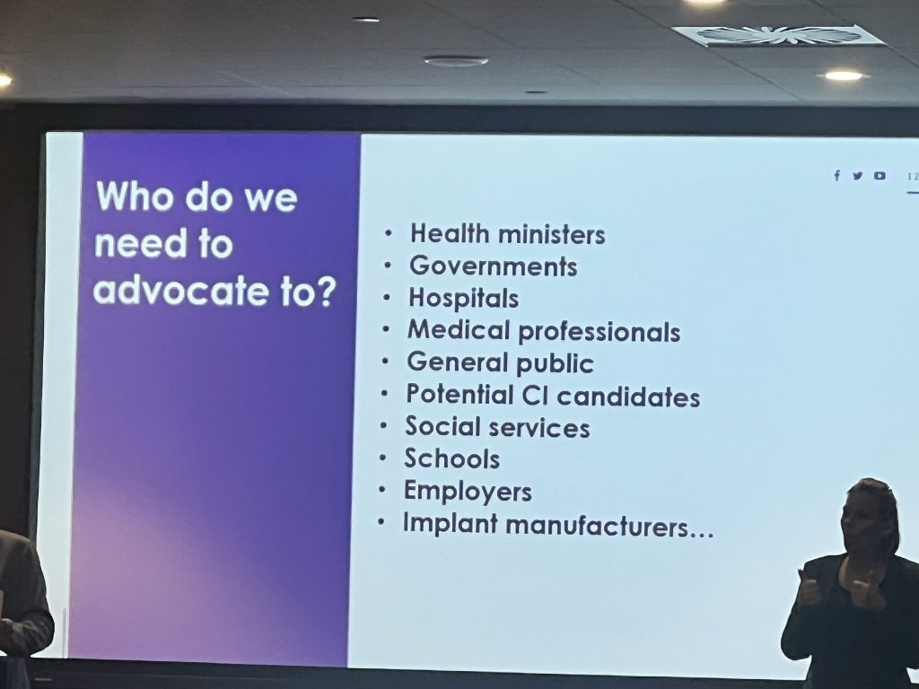 Lähikuva esitysdiasta näytöllä, kuvassa lukee "What do we need to advocate to? Health ministers, governments, hospitals, medical professionals, general public, potential CI candidates, social services, schools, employers, implant manufacturers"