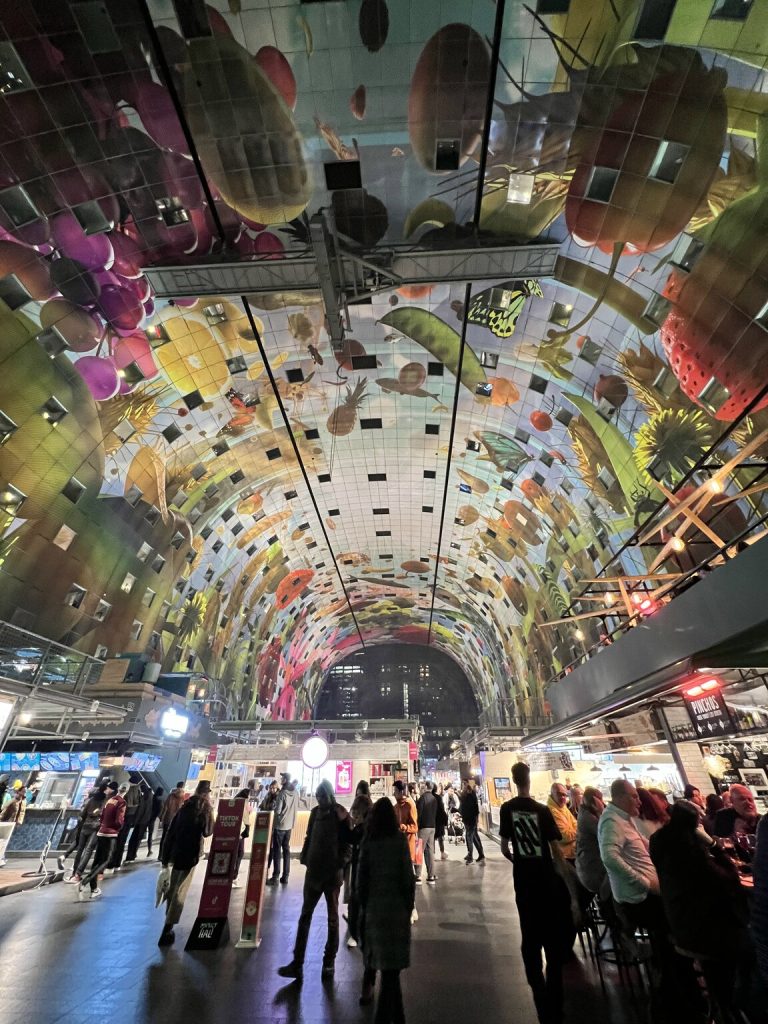 Kuva otettu Rotterdamin Market Hallin sisältä, kaarevaan seinään on heijastettu erilaisia pyöreitä kuvioita. Edessä näkyy paljon ihmisiä