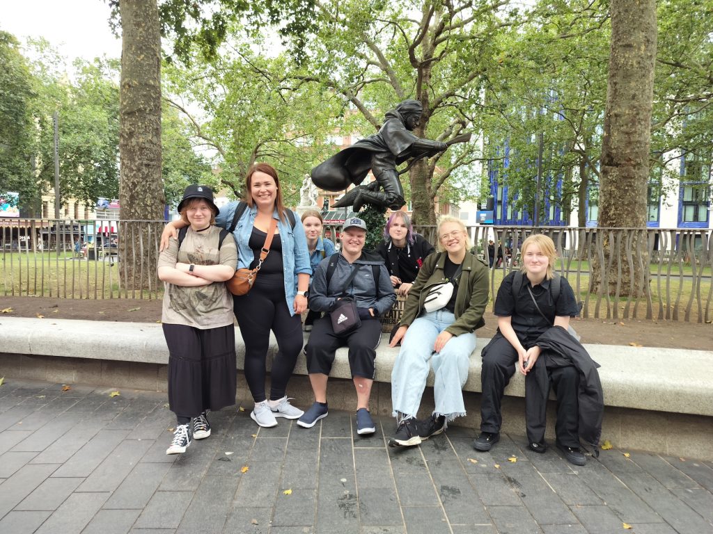 Ryhmäkuva Potter-kierroksen osallistujista Harry Potter -aiheisen patsaan edessä. Takana näkyy puistoa ja taloja. 