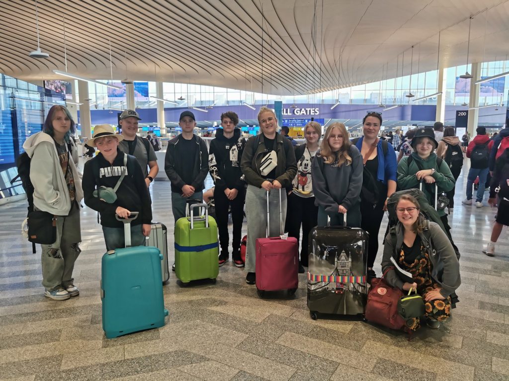 Ryhmäkuva kielimatkalle lähteneistä nuorista ja ohjaajista matkalaukkujen kanssa Helsinki-Vantaan lentokentän aulassa