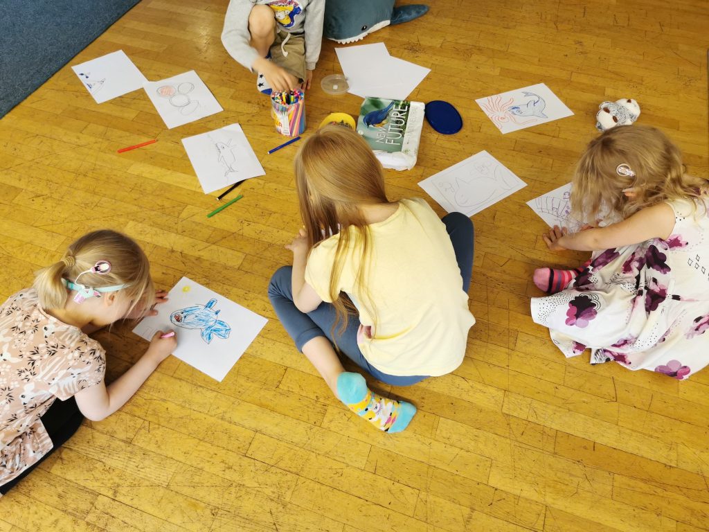 Lapsia piirtämässä lattialla, osalla lapsista näkyy sisäkorvaistute.