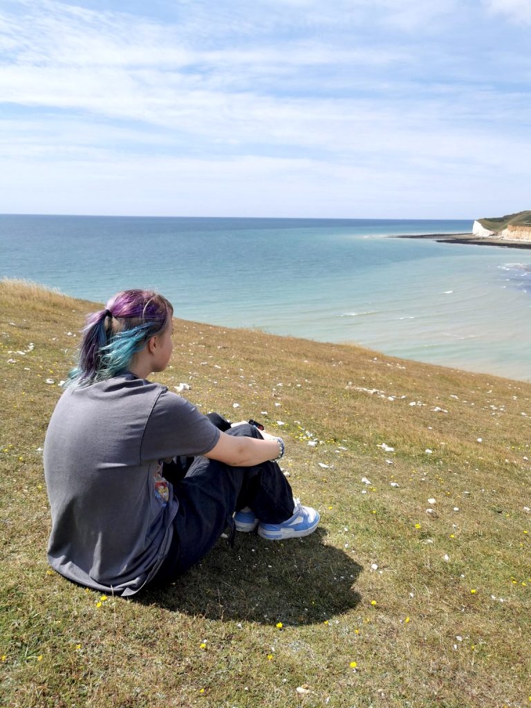 Nuori istuu rinteellä selkä viistosti kameraan ja katsoo merelle.