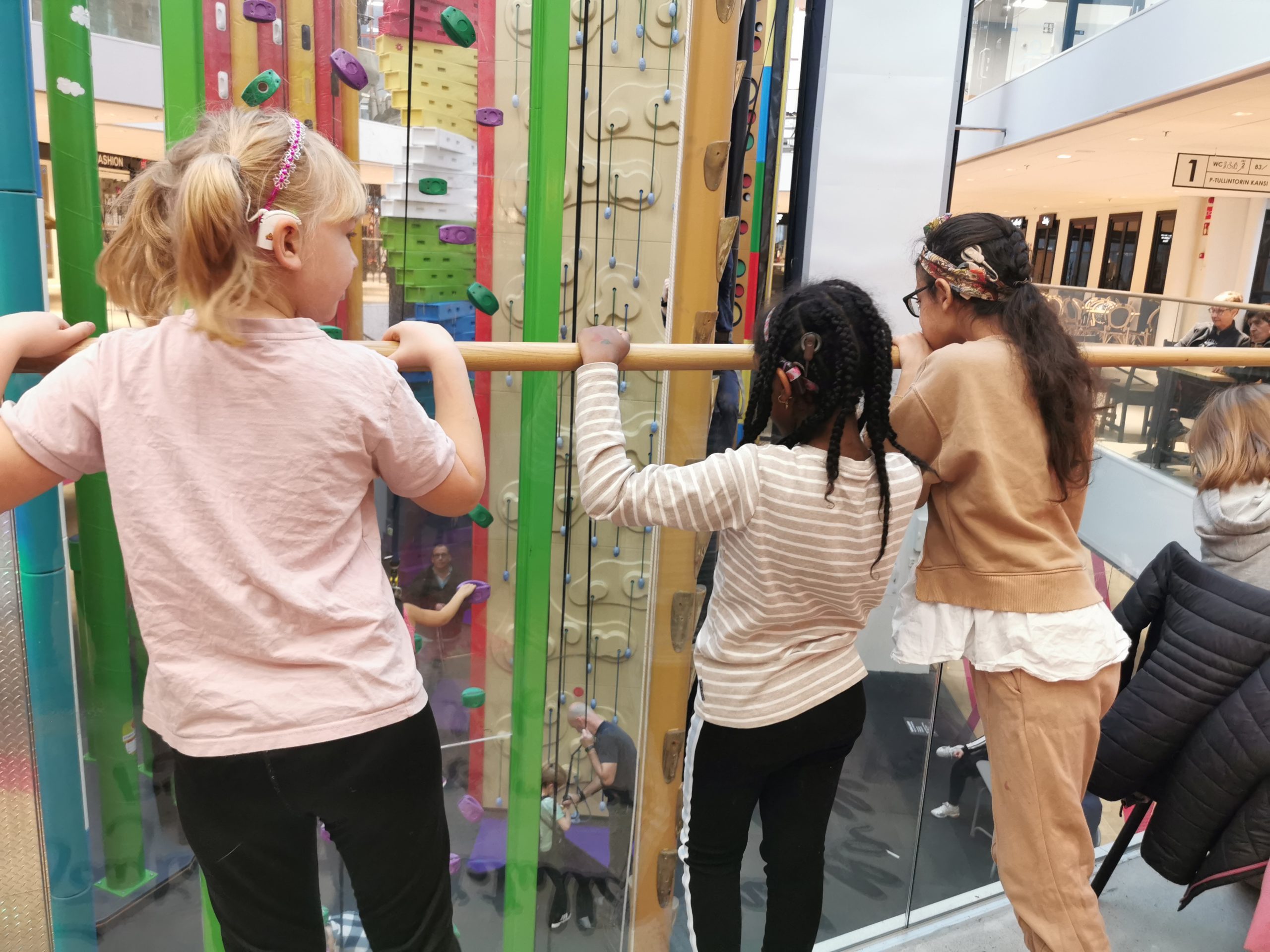 Kolme SI:ta käyttävää lasta katselee korkeita kiipeilyseiniä.