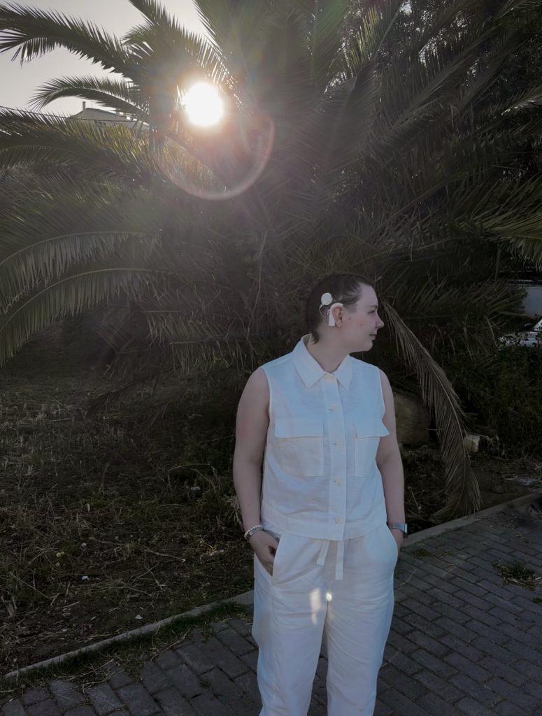 Helmi seisomassa palmun edessä katse oikealle, valkoinen SI näkyy selkeästi korvassa.