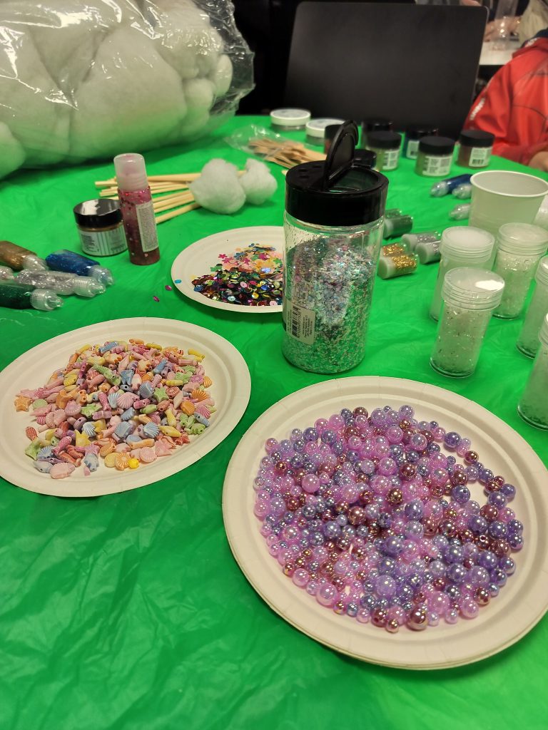 Lähikuvassa pöydälle asetellut koristehelmet, glitterit ja muut askarteluvälineet.