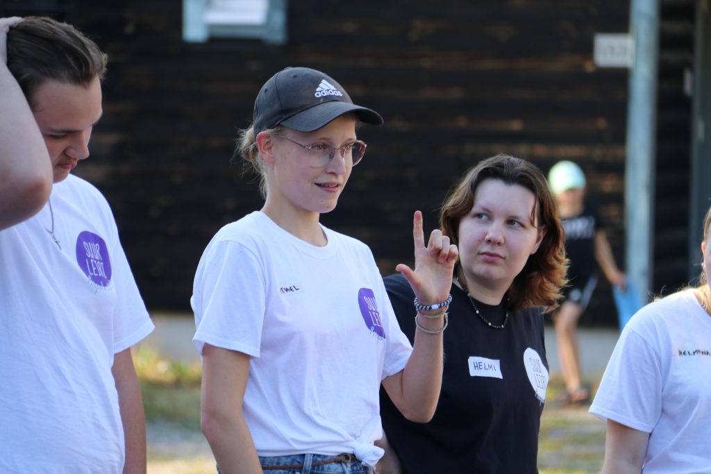 kolme ihmistä seisoo vierekkäin, kahdella on valkoinen paita ja yhdellä musta. 
