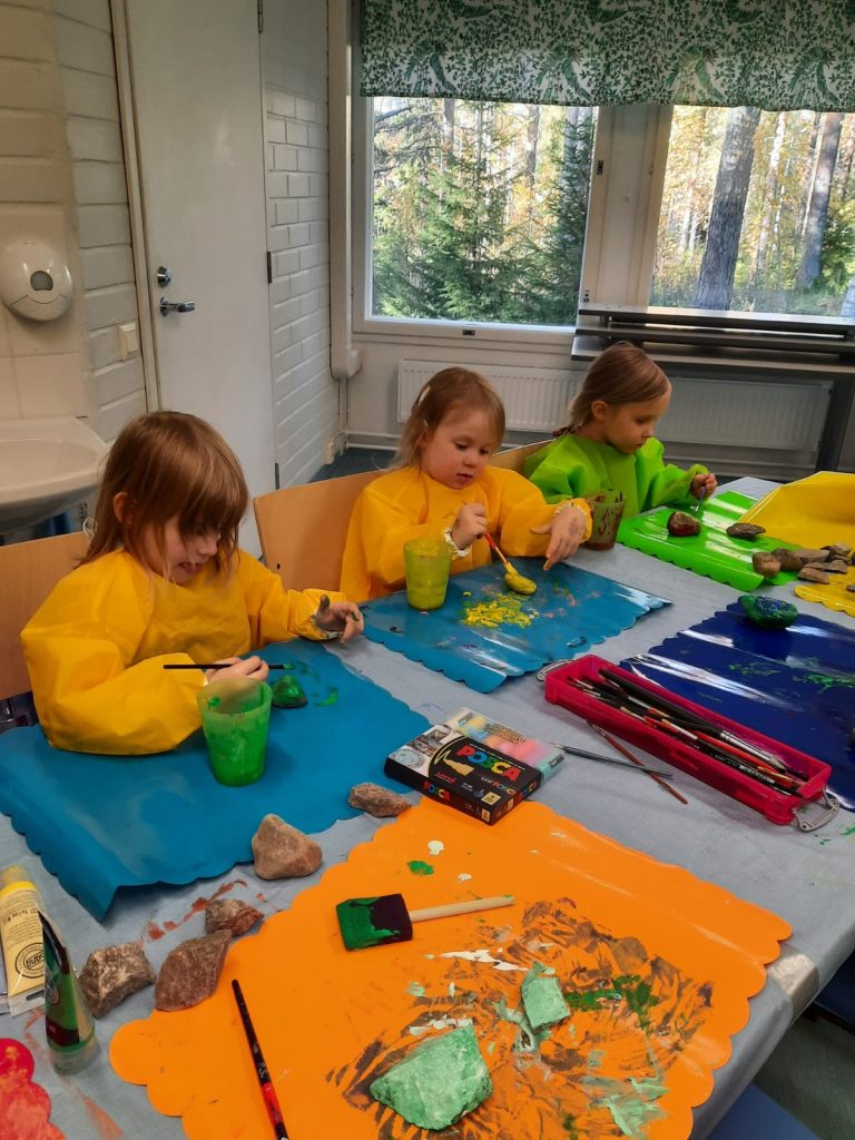 Pieniä lapsia pöydän ääressä maalaamassa kiviä.
