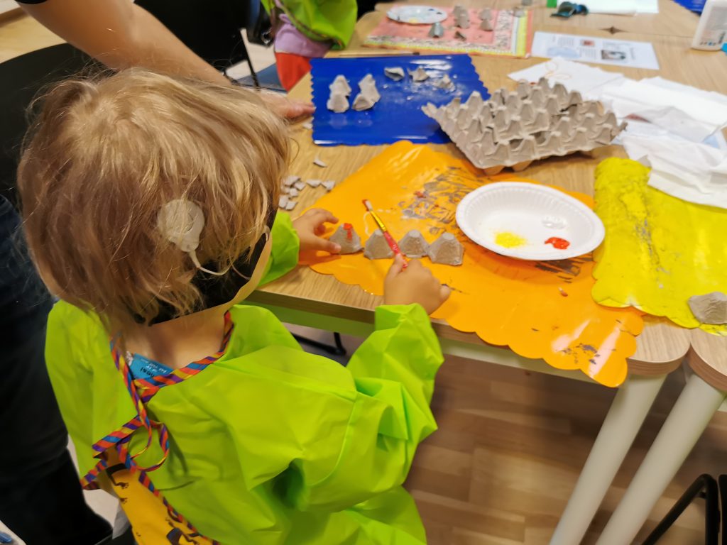 Pieni SI:ta käyttävä lapsi maalaa pöydän ääressä kananmunakennoa.