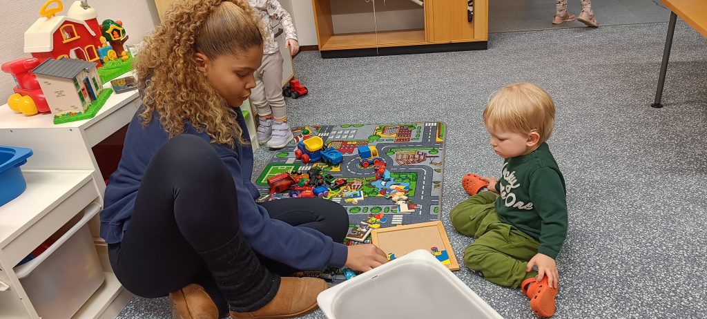 lastenhoitaja ja pieni lapsi istuu lattialla tekemässä yhdessä palapeliä