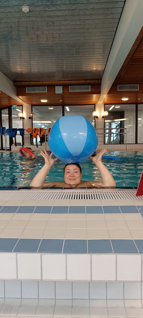 Ihminen uimassa ja pitelee isoa palloa päänsä päällä. 