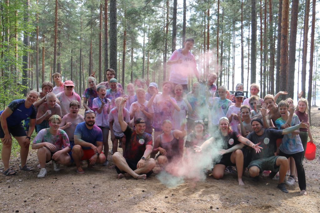 Yhteiskuva suurleiriltä. Kuvassa ohjaajat ja leiriläiset sekä värijauhetta ilmassa väriestejuoksusta.