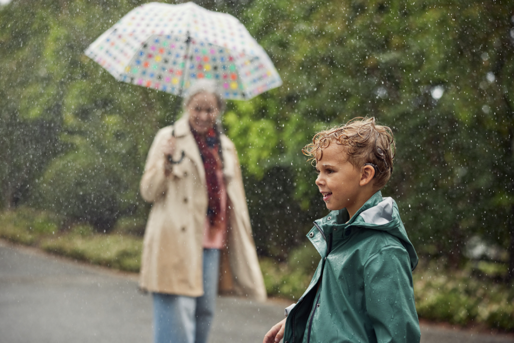 Pieni poika ja nainen ovat ulkona sateella. Pojalla on Nexa-järjestelmän puheprosessori.