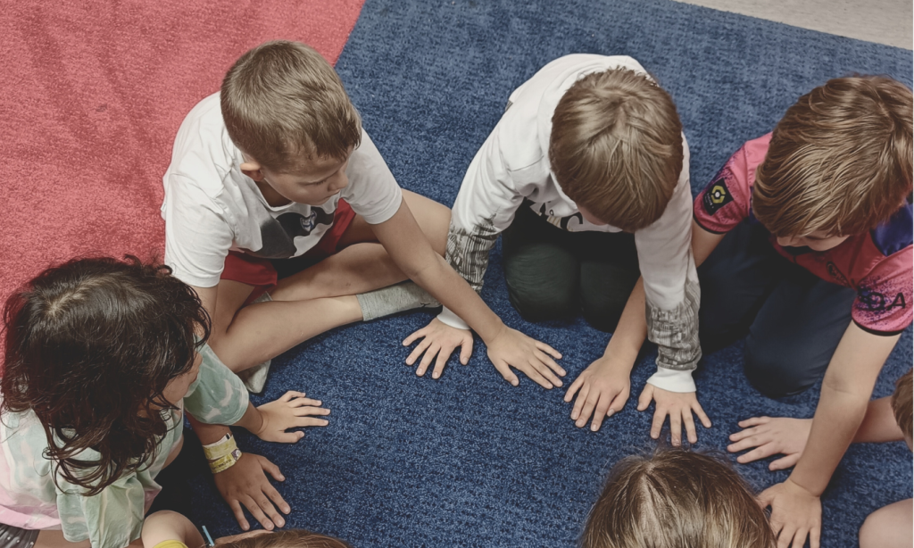 Lapsia istuu lattialla ringissä pelaamassa läpsyä.