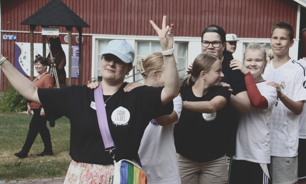 Ohjaajia ja nuoria jonossa, kädet toistensa olkapäillä. Etutalan ohjaaja näyttää voitonmerkkiä.