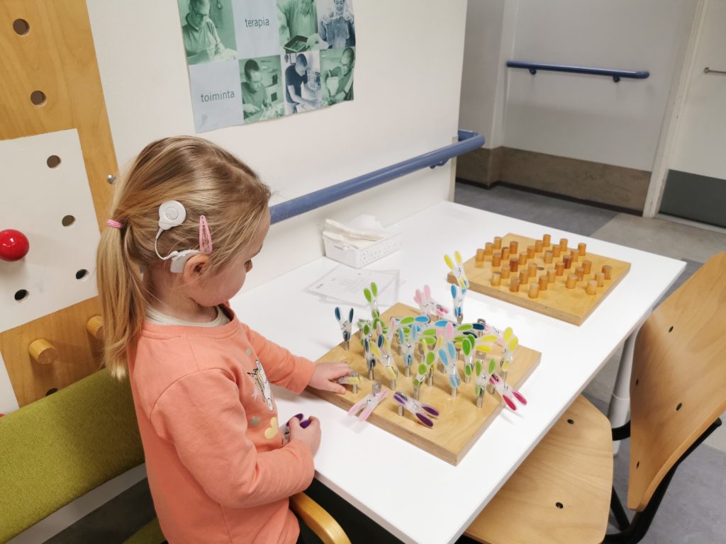 Pieni lapsi leikkii pöydän ääressä. Lapsella on sisäkorvaistute.