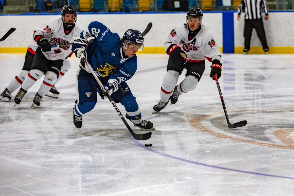 Suomen ja Kanadan pelaajia jäällä taistelemassa kiekosta.