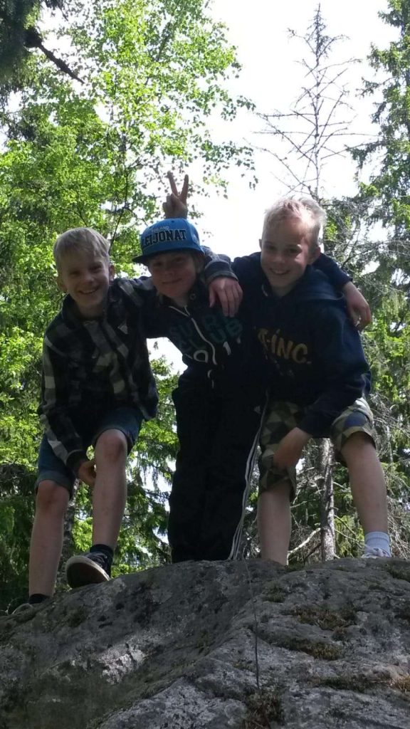 Kolme hymyilevää poikaa poseeraa kalliolla. 